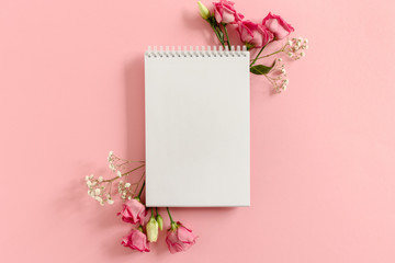 Open notepad mockup with frame made of flowers on pink pastel background