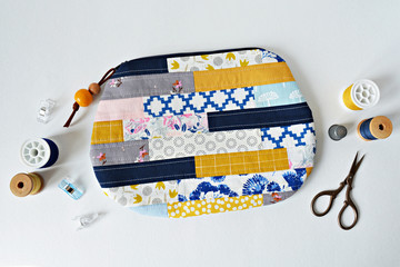 Patchwork quilted makeup bag with wooden beads, thread, scissors and clips over white