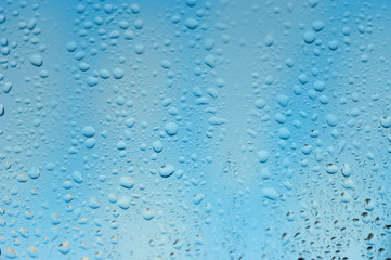 viele kleine Wassertropfen auf einer Scheibe in blau bei Regen