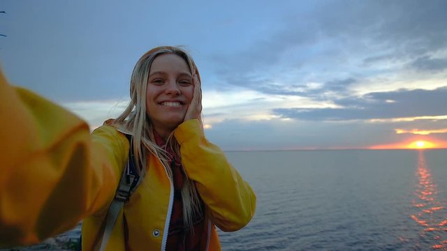 Attractive, happy and emotional blonde woman taking video selfie on the smartphone. Shooting amazing sunset over the sea.