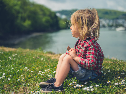 Little toddler sitting on the grass by water with fruit bar