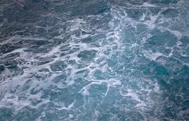 blue ocean waves creating white foam seen from above.