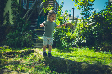 Little toddler balancing on log in park