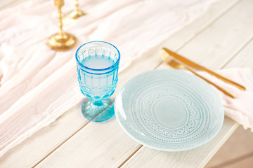 Table for guests, decorated with candles, served with cutlery and crockery and covered with a tablecloth blue plate and golden fork and knife on pink gauze napkin.