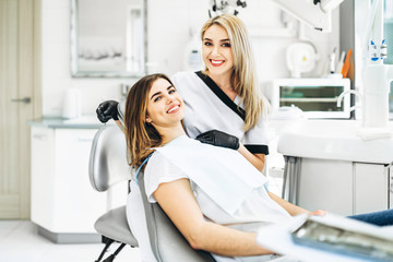 Pretty young female dentist making examination and treatment for young female patient in dental clinic.