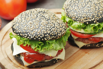 Two black burgers with vegetables and beef meat