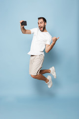 Full length photo of optimistic caucasian man in casual white t-shirt rejoicing while jumping and...