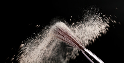 Fine art cosmetic, makeup concept with a highlighted soft bristle brush and a puff of facial powder...