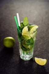 Mojito Cocktail with Lime Mint in Vertical Glass on Black Stone Background. Green Summer Fresh Mohito with Straw and Ice. Fruit Soda Beverage. Cold Cuban Alcoholic Gin for Restaurant Bar