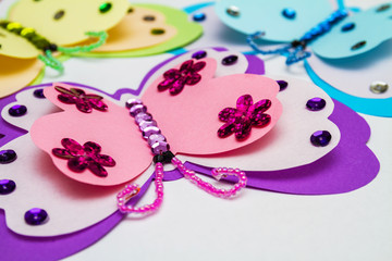 Application made with hot melt glue gun. Three butterflies made of colored paper, multi-colored sequins, paillettes and beads. Closeup, selective focus