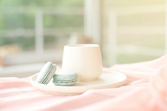 French blue macaroon and coffee cup standing on a wooden table with a pink tablecloth white vase with flowers roses and greens.