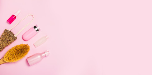 Spa cosmetic background. Bottles, body brush and tropic leaves on pink background. Top view, flat lay.