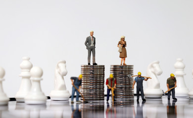 The chess pieces on the chessboard and miniature people. Piles of coins and miniature people.