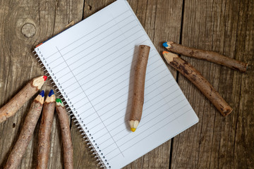 Pencils made of branches and a notebook on a wooden background