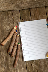 Pencils made of branches and a notebook on a wooden background