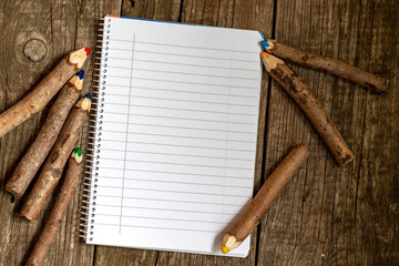 Pencils made of branches and a notebook on a wooden background