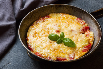 Omelet, scrambled eggs with tomatoes and cheese in a pan on a dark table.