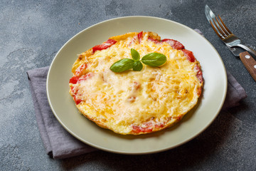 Omelet, scrambled eggs with tomatoes and cheese in a plate on a dark table.