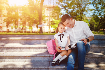 first day at school. Father and little kid daughter sitting on stairs and read book, study lessons. Parenthood and child concept.