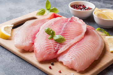 Raw fish fillet of tilapia on a cutting Board with lemon and spices. Dark table