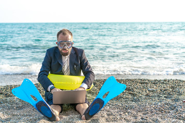 Successful businessman wearing snorkeling tools is working on the beach with laptop