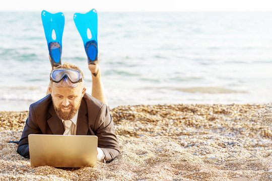 Successful businessman wearing snorkeling tools is working on the beach with laptop