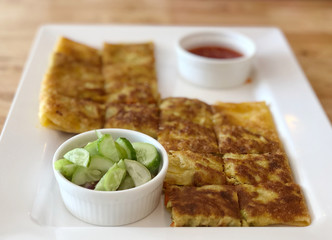 Roti mataba and sauce cup in white plate with hot tea glass on the wooden table, serving size and  Natural light.