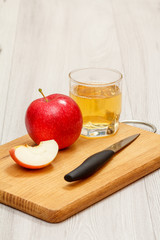 Glass of apple juice with red apple and knife on wooden cutting board,