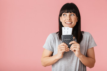 Excited happy woman posing isolated over light pink background wall holding passport with tickets.