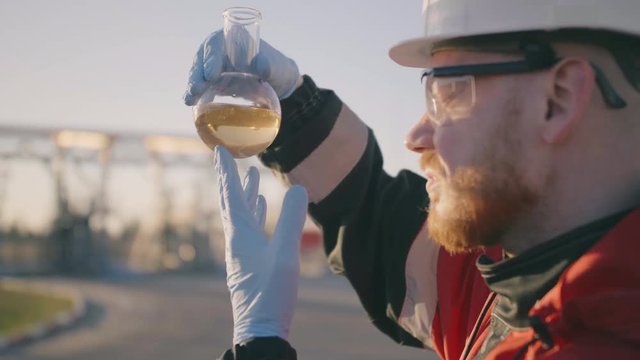 Side view of petrochemical engineer who examines petroleum oil in flask