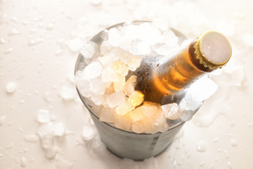 Beer bottle in metal bucket full of ice cubes on white table