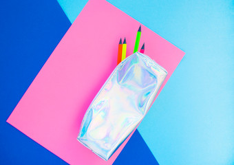 Colorful paper, neon pencils and holographic pencil case on blue and pink background. Flat lay style. Back to school concept.