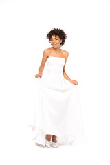 happy african american bride smiling while touching wedding dress isolated on white