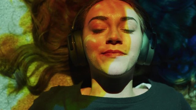 Close up of woman laying on floor listening to headphones illuminated by flowing colors / Cedar Hills, Utah, United States