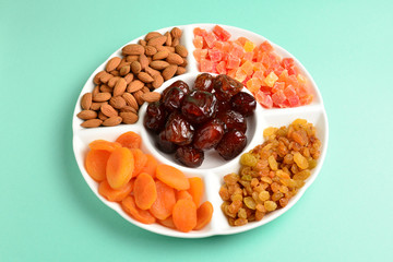 Mix of dried fruits and nuts on a white plate. Apricot, almond, raisin, dates fruit. On a green background. Space for text or design.