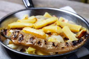 Delicious roast potatoes with onion and spices in a pan on kitchen towel on the old wooden table. Traditional rural dinner