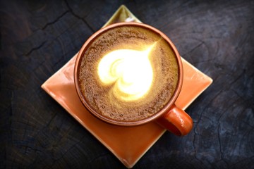 Hot coffee latte on a wooden heart-shaped makeup.