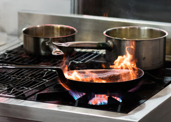 Chef cooking with flame in a frying pan on a kitchen stove.