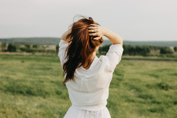 Beautiful carefree long hair girl in white clothes enjoys life in the nature field, view from back....