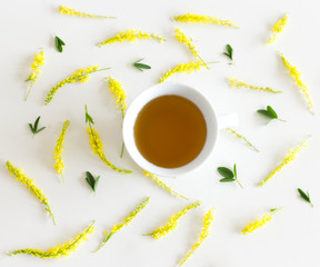 Herbal tea in a porcelain cup.Melilotus officinalis, known as yellow sweet clover on white table. Used in herbal medicine.