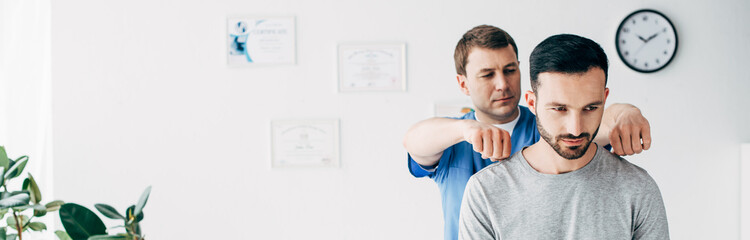 panoramic shot of chiropractor massaging neck of handsome man in hospital