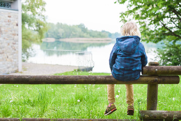 Ein Junge sitzt auf dem Zaun.Am See.
