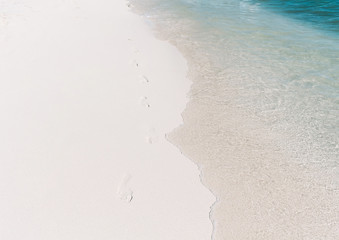 Footprints on the white sand of the beach along the wave. Summer vacation concept.