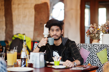 Beard asian man in casual wear sitting indoor cafe and drink coffee.