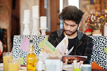 Beard asian man in casual wear sitting indoor cafe and read menu.