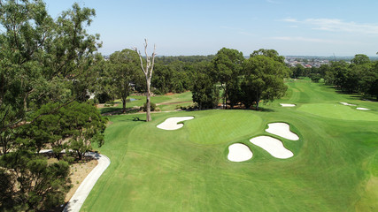 Obraz premium Aerial drone view golf course green with sand bunkers, flag, trees, green grass against blue sky