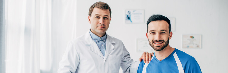 Obraz premium panoramic shot of smiling Physiotherapist in white coat and patient looking at camera in hospital