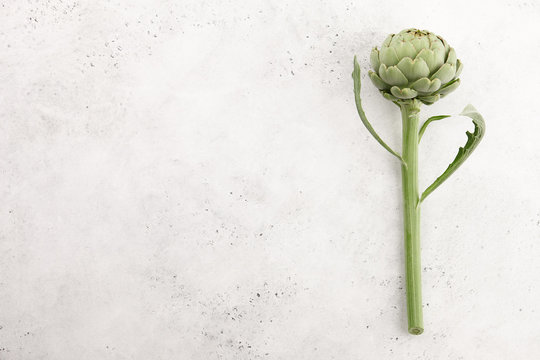 Fresh green artichoke with stem and leaves on white stone background, top view
