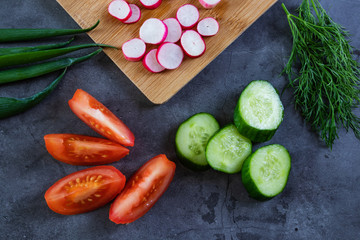 Fototapeta na wymiar Vegetables for salad: cucumbers, tomatoes, radishes, green onions and dill. Dark background. Wooden cutting board.The concept of vegetarianism, healthy eating, food rich in vitamins. Fresh harvest. 