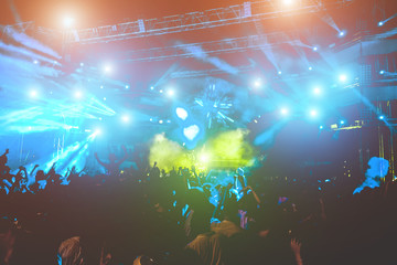 Happy people dancing and having fun in summer music festival party outdoor - Crowd celebrating concert event - Soft focus on center hand up with green flare in background - Fun and youth concept